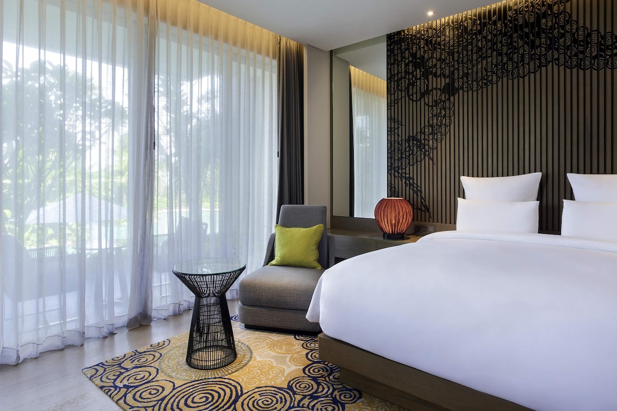 Een moderne hotelkamer met een groot bed, een stoel, een klein tafeltje en een decoratief wandpaneel.