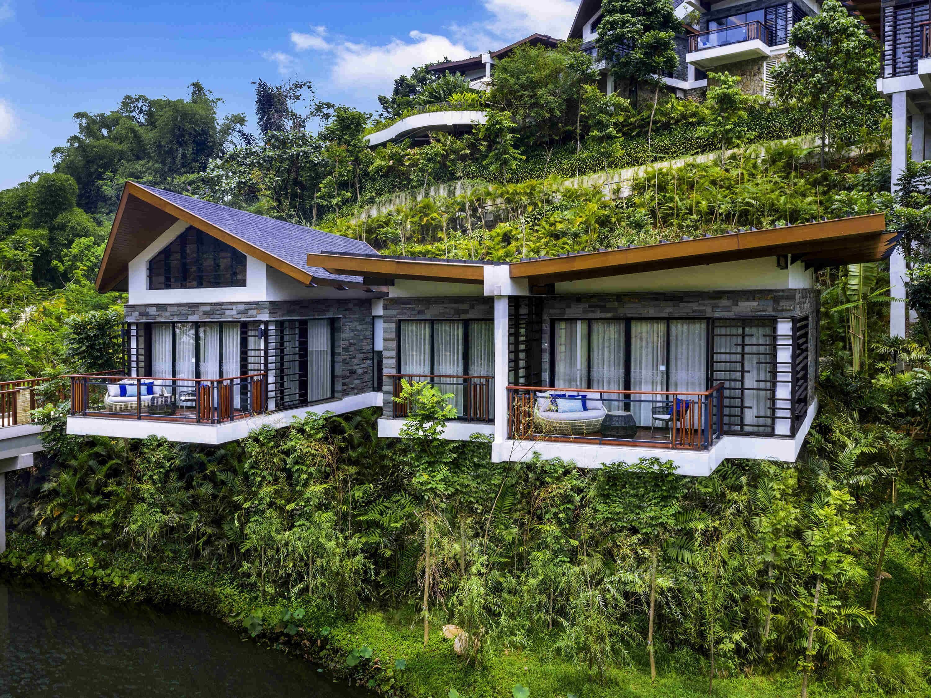 A modern house with two balconies overlooking a lush garden and a river.