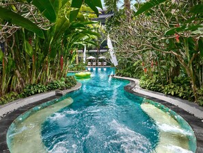 Una piscina rodeada de exuberante vegetación tropical y un área junto a la piscina de color azul cristalino.