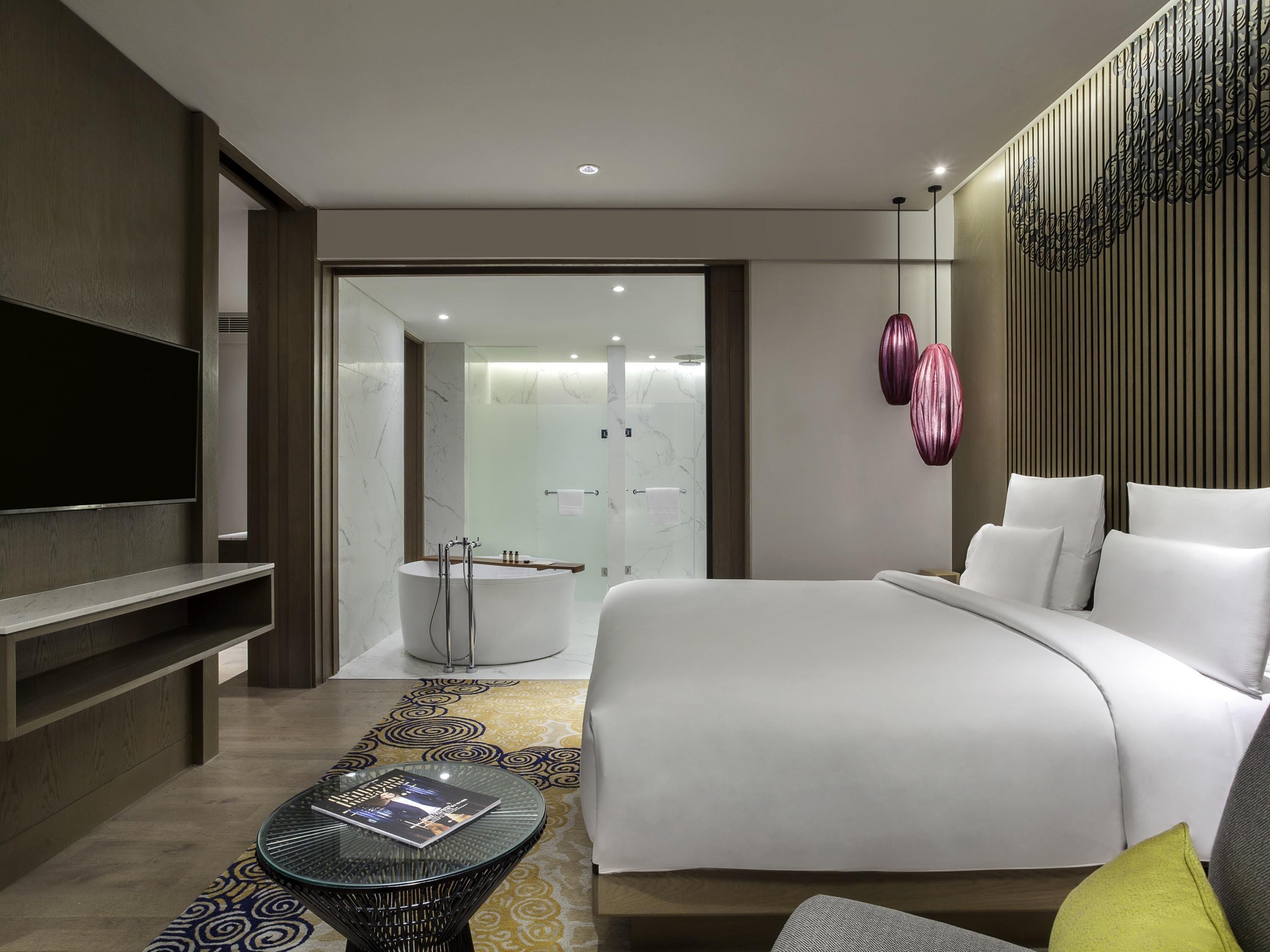 Une chambre d’hôtel moderne dotée d’un grand lit, d’une télévision, d’une table basse en verre et d’une salle de bain avec baignoire.