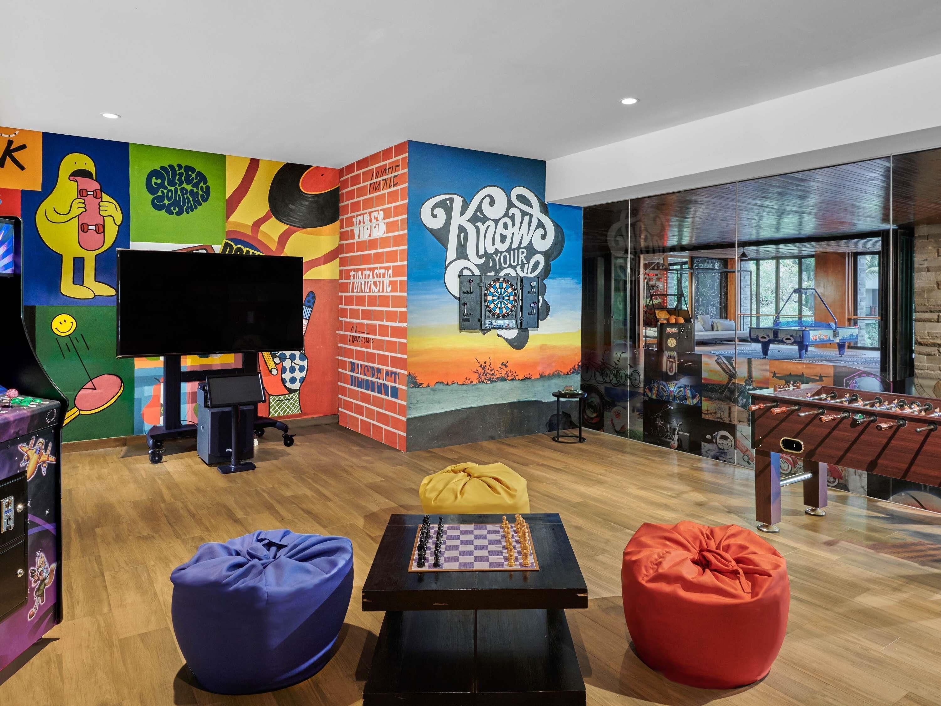 A vibrant room with a large mural, a dartboard, a foosball table, and bean bag seating.
