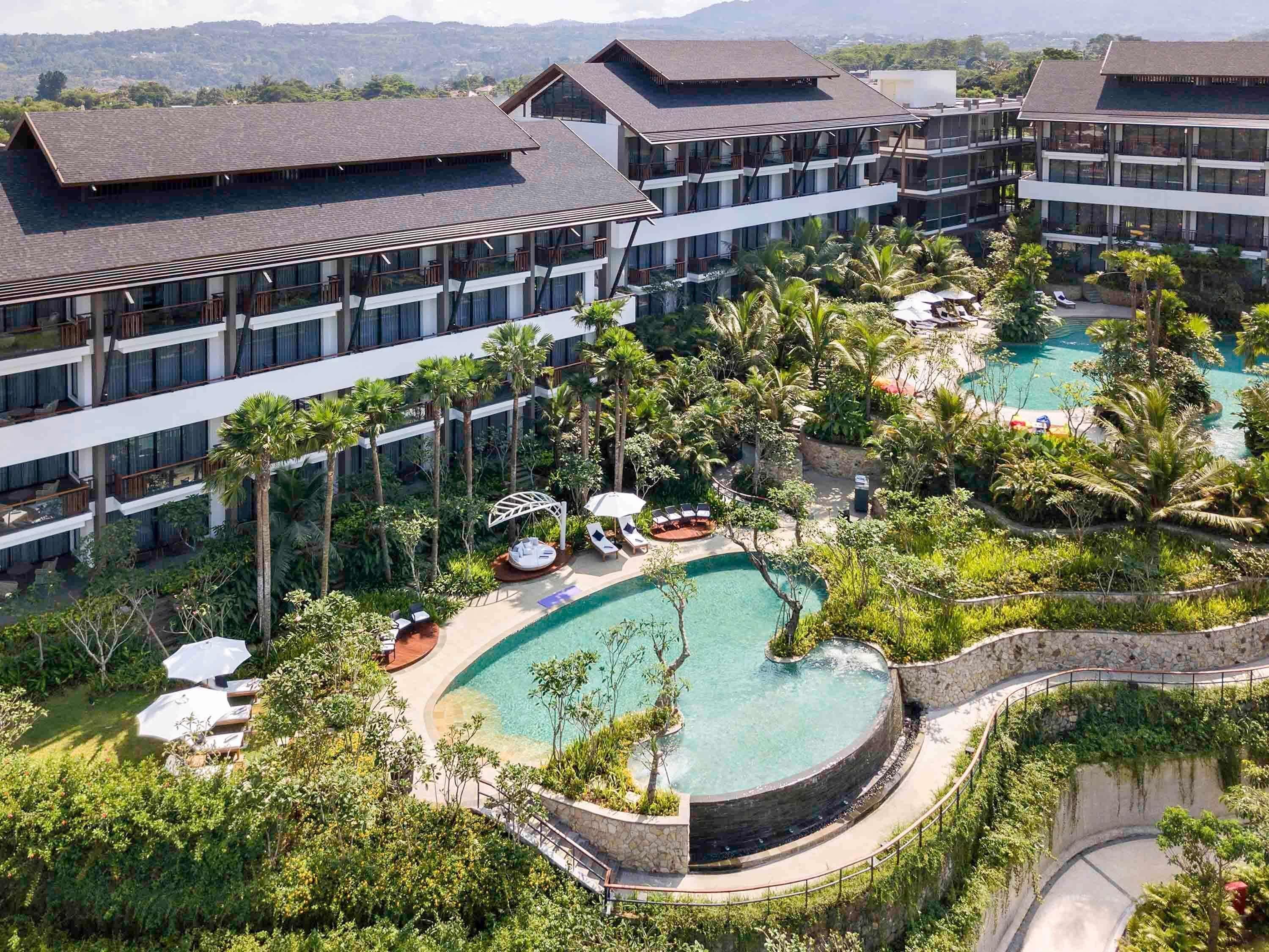A hotel with multiple floors, outdoor swimming pools, and lush greenery.
