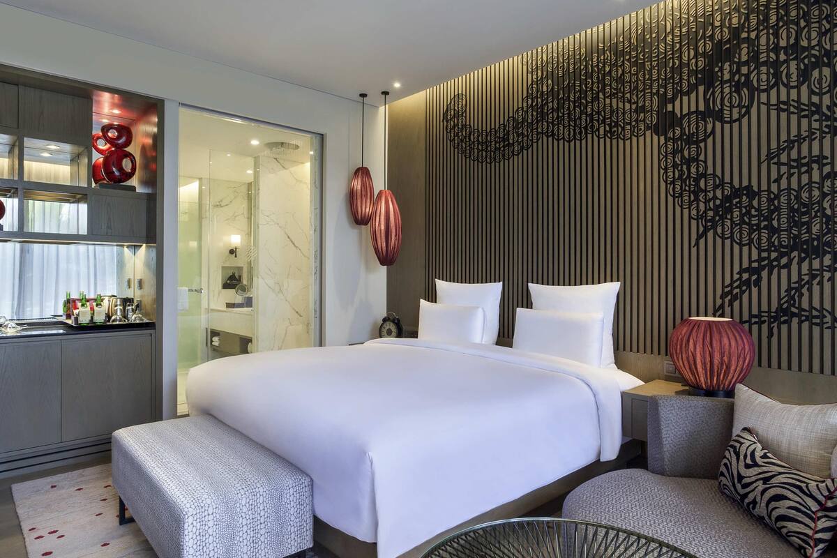Une chambre d’hôtel moderne dotée d’un grand lit, d’un coin salon, d’une cloison en verre et d’un panneau mural décoratif.