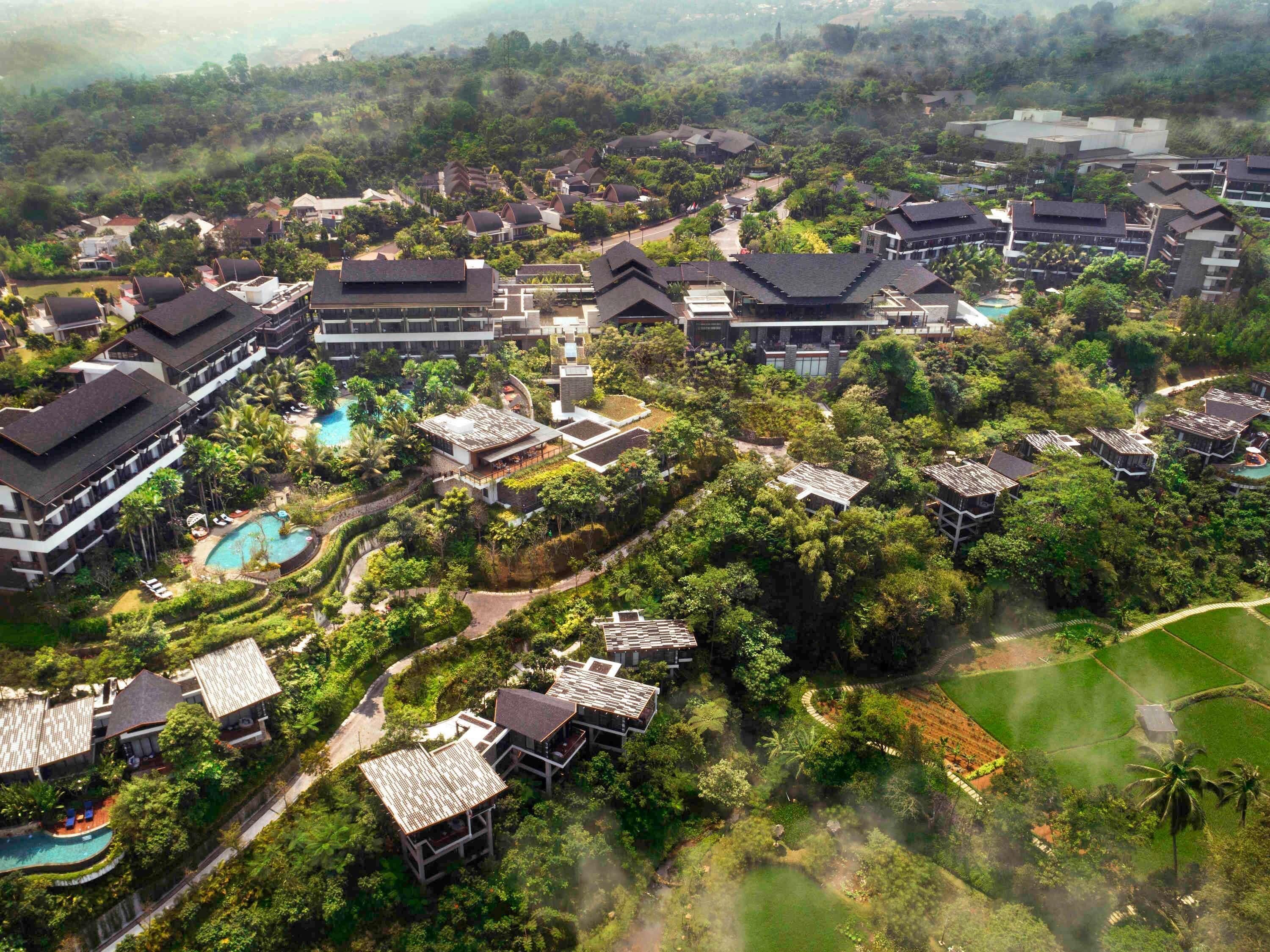 Vista aérea de un resort con varias construcciones, una piscina y exuberante vegetación.