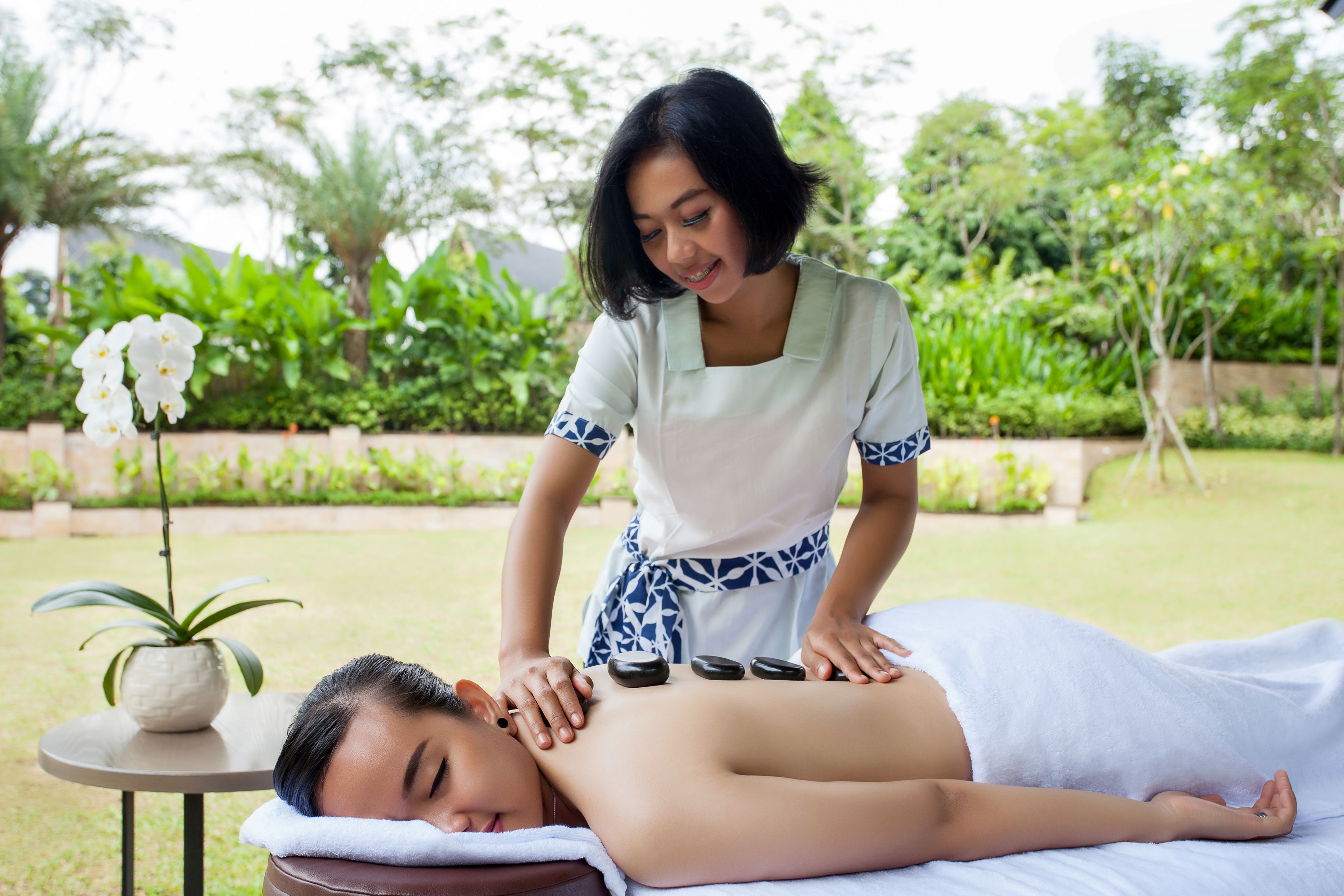 A person receiving a massage outdoors with a potted plant and greenery in the background.