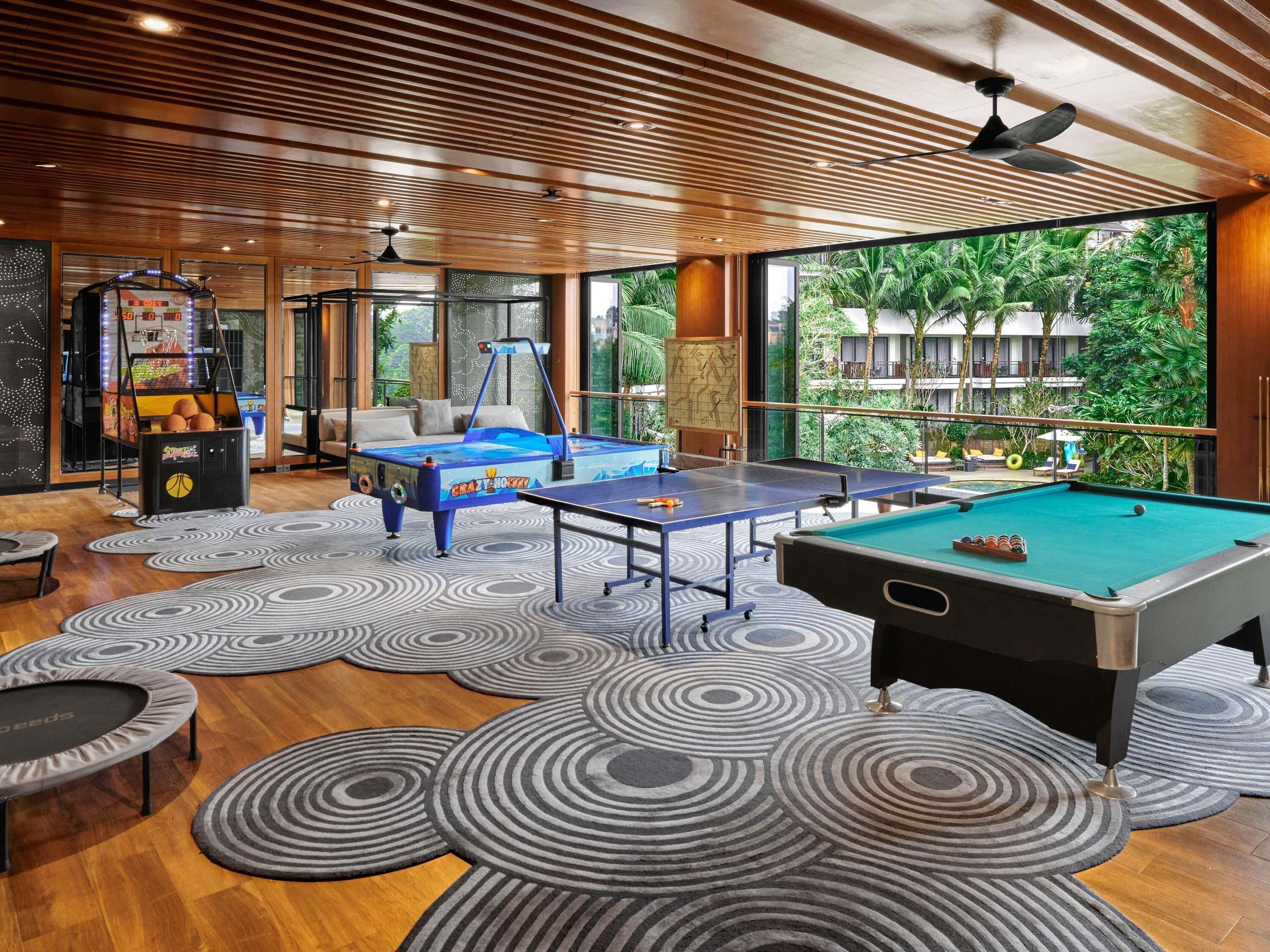 A pool table, a ping pong table, and a foosball table in a room with a wooden ceiling and large windows.