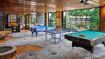 A pool table, a ping pong table, and a foosball table in a room with a wooden ceiling and large windows.