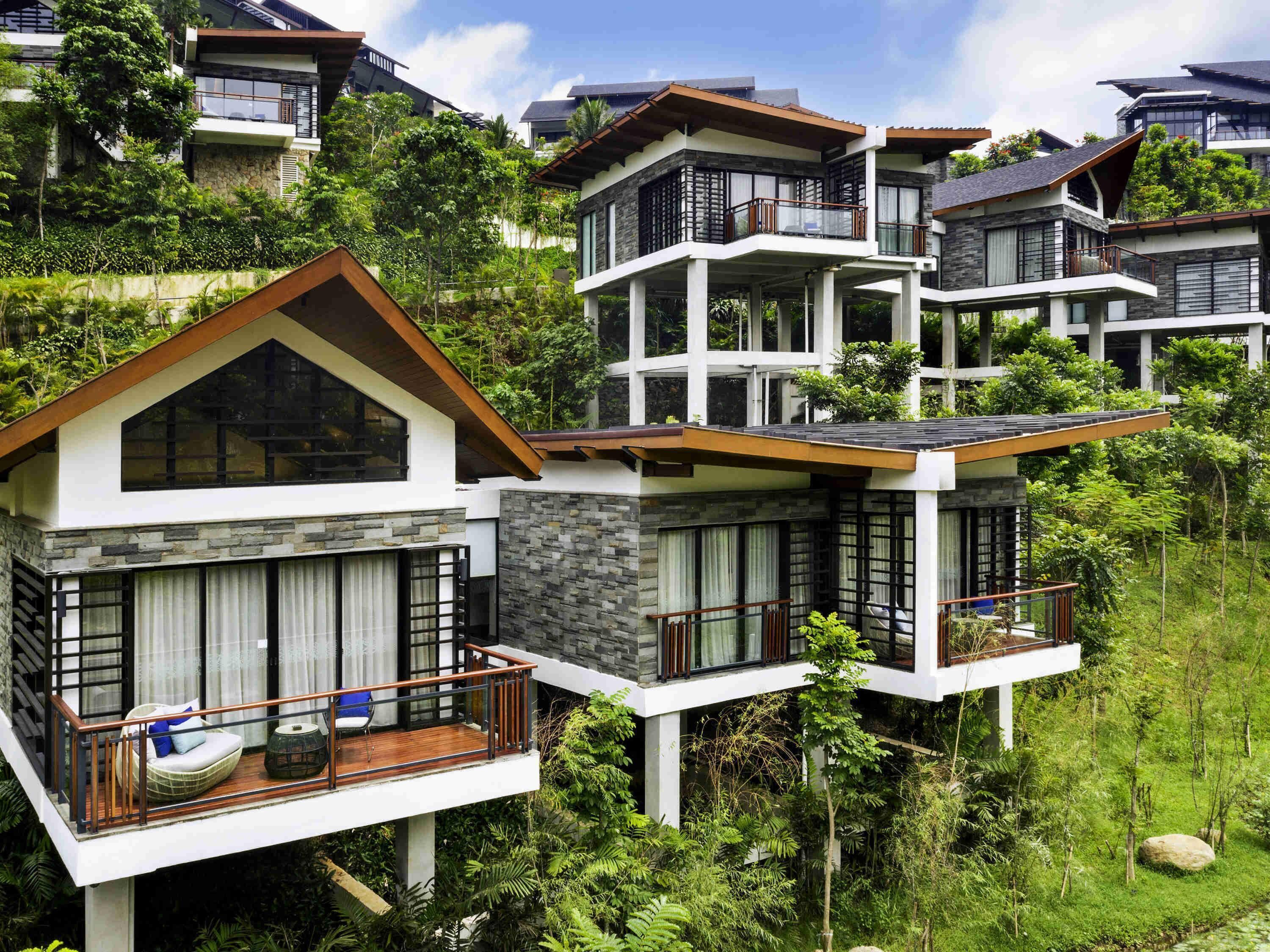 A modern multi-story residential building with balconies, large windows, and a lush green environment.
