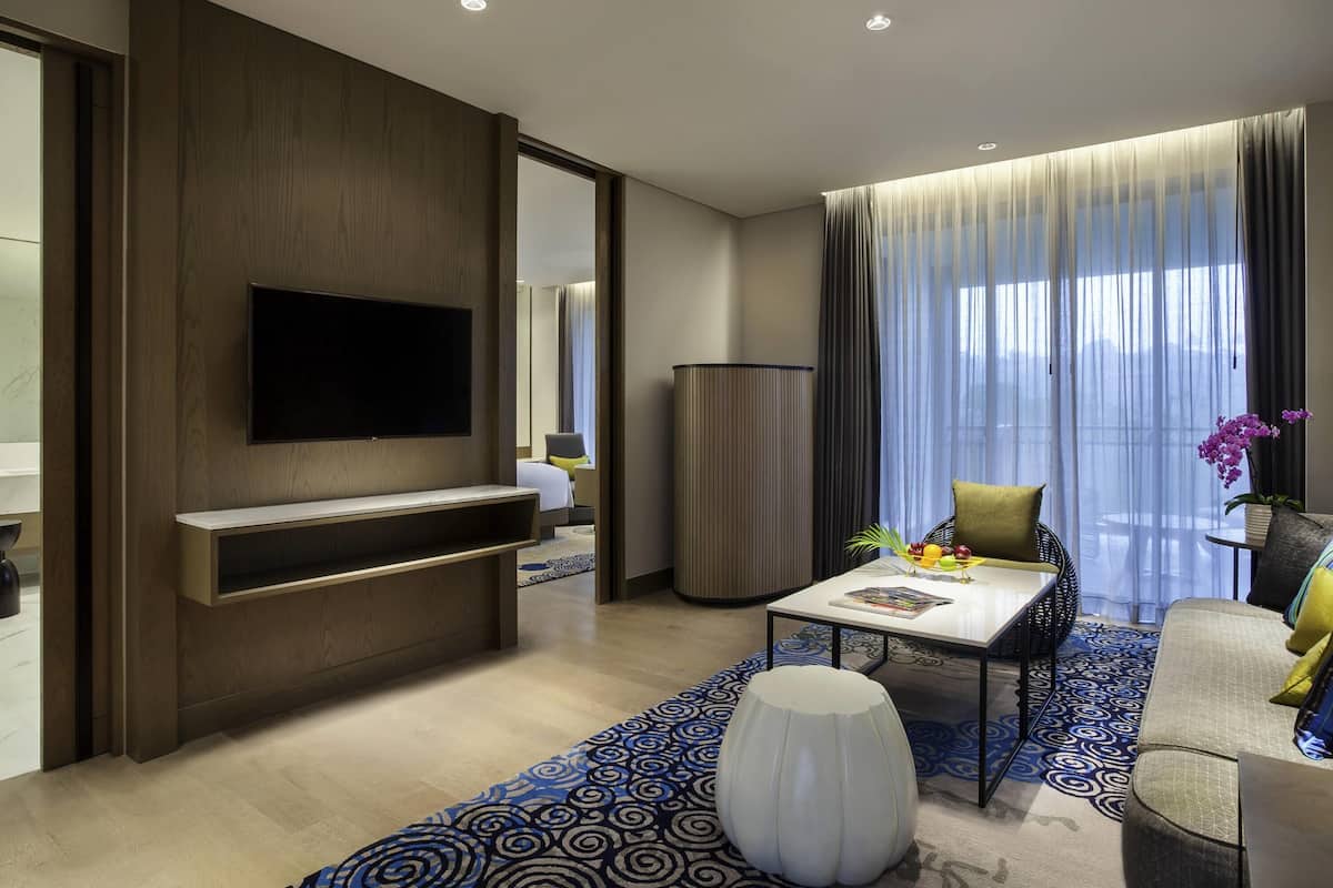 Une chambre d’hôtel moderne dotée d’un téléviseur à écran plat fixé sur un panneau en bois, d’un canapé, d’une table basse et d’un tapis à motifs.