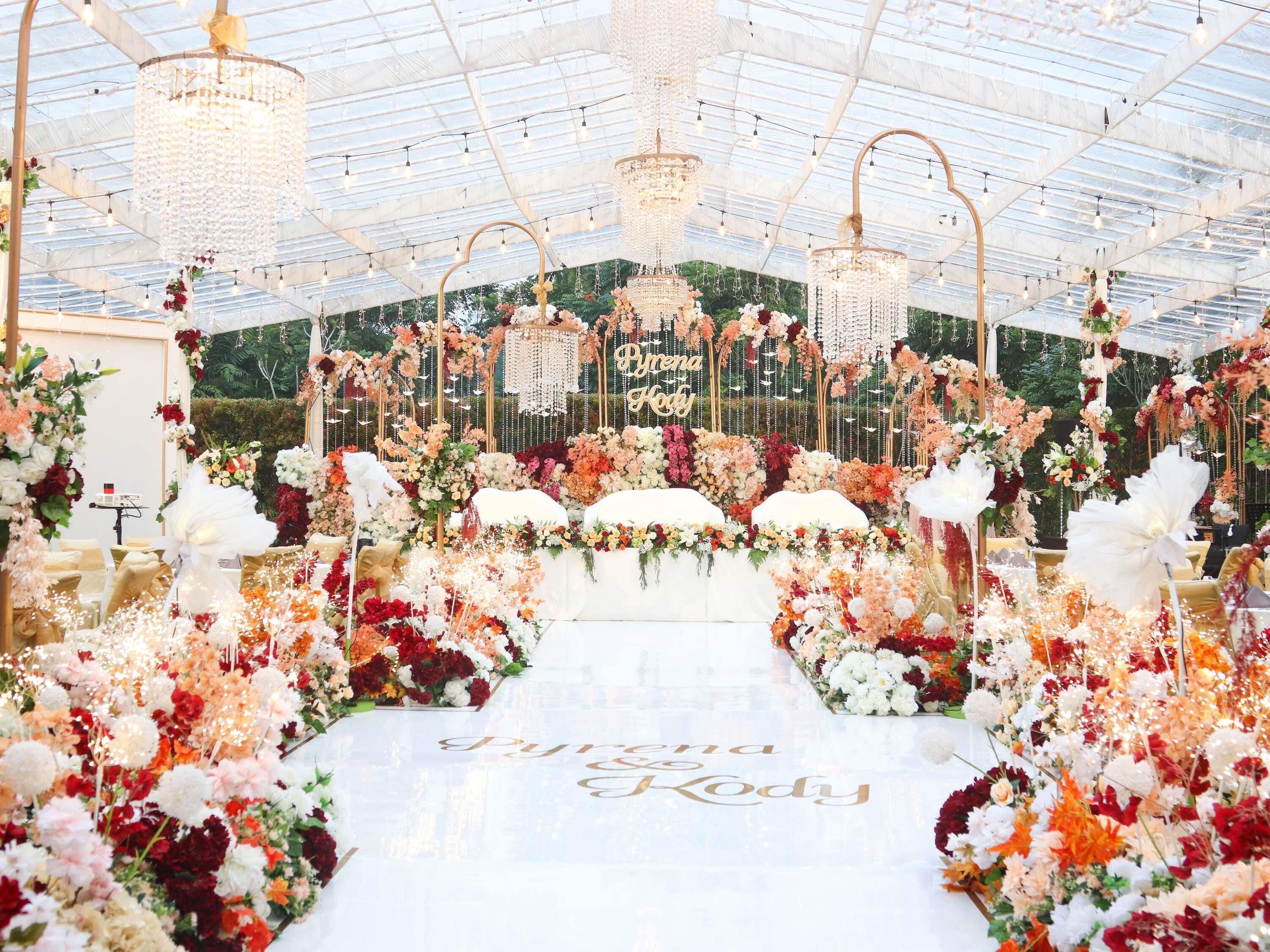 An indoor venue with a glass ceiling, floral decorations, and a stage with 'Pyriona & Kody' written on it.