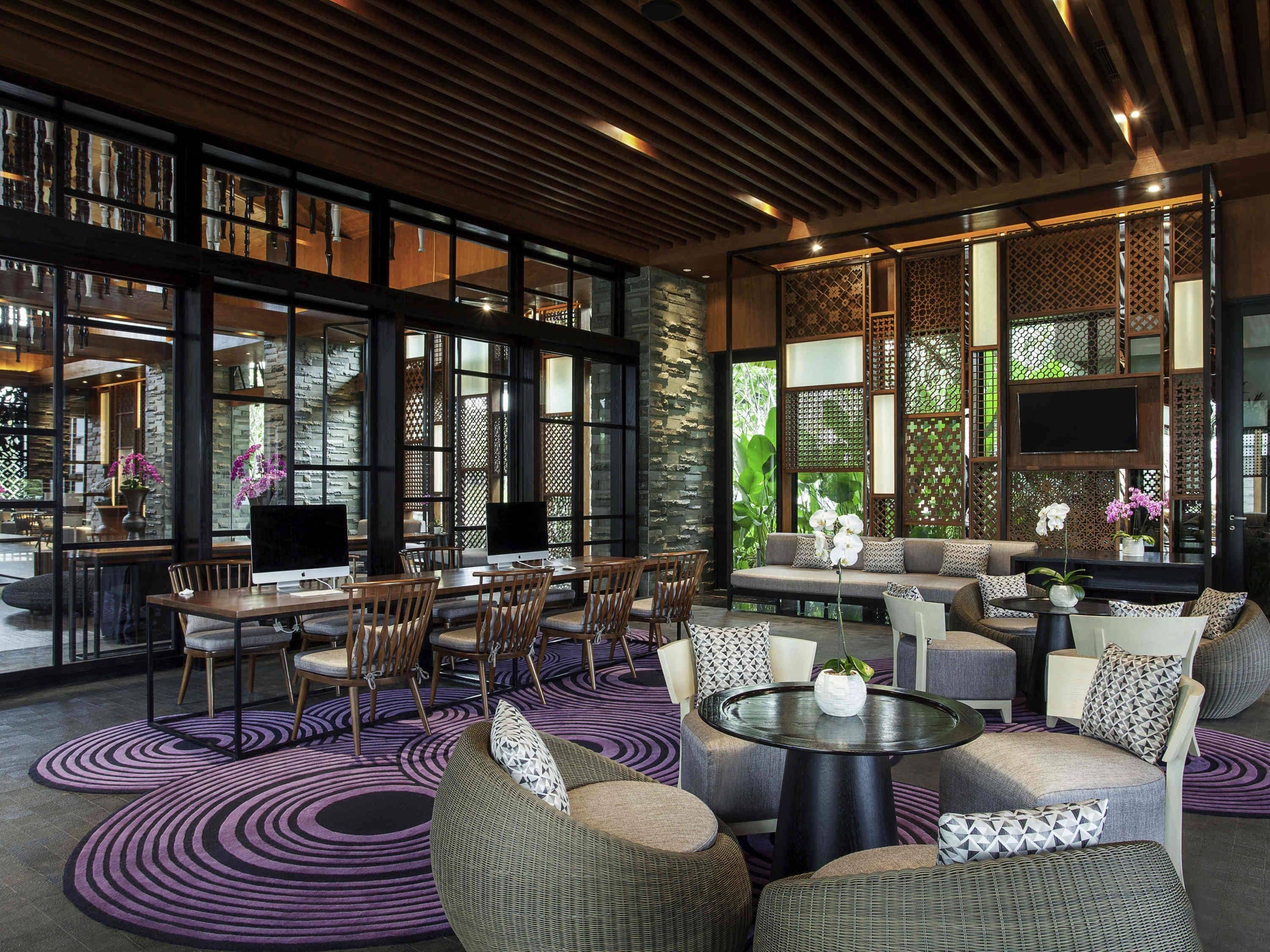 A modern lounge area with a mix of seating options, including sofas and chairs, arranged around a central coffee table. Large windows provide ample natural light and views of the outdoors.