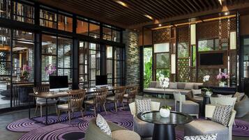 A modern lounge area with a mix of seating options, including sofas and chairs, arranged around a central coffee table. Large windows provide ample natural light and views of the outdoors.