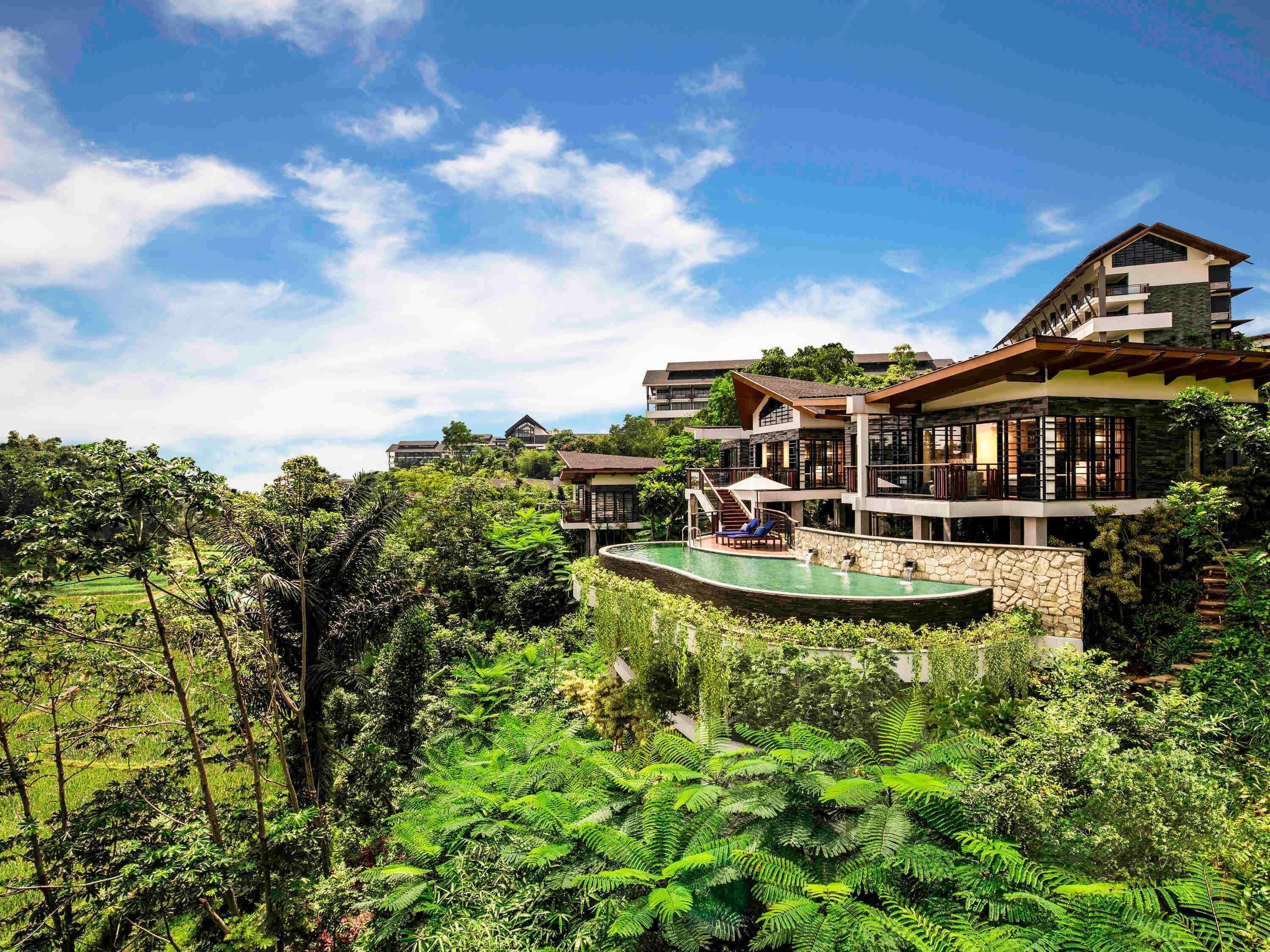A multi-story resort with a pool surrounded by lush greenery.