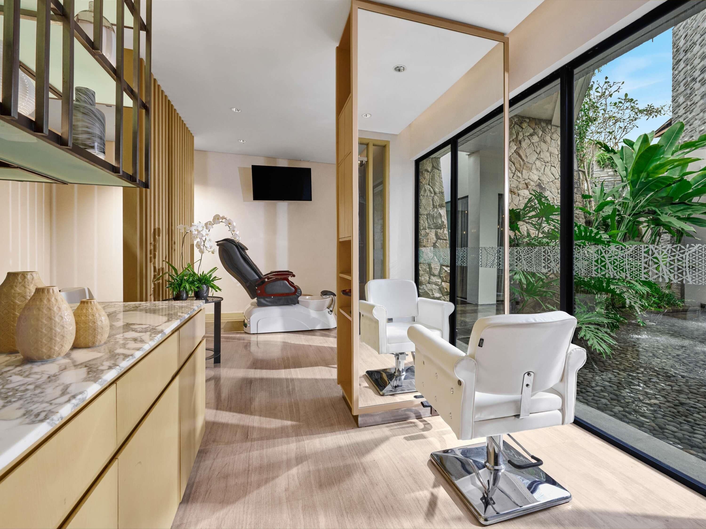 Un spa moderno con una silla de masaje, una mesita pequeña y un ventanal con vistas a un jardín.