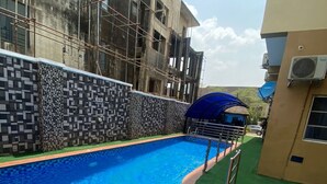 A swimming pool with a tiled edge, a metal ladder, and a green artificial turf area. - Degok Hotel (Abuja)