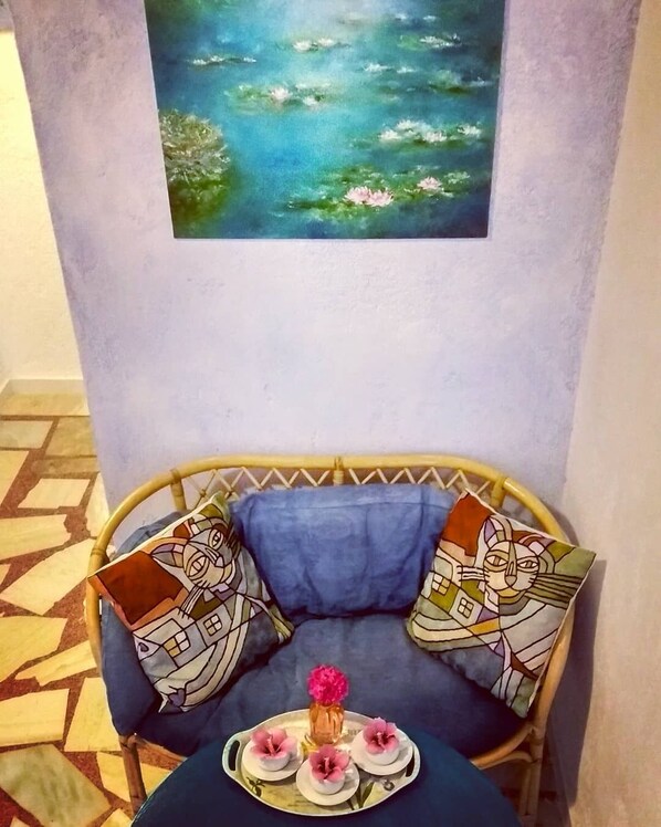 A room with a blue sofa, a painting of a pond, and a tray with pink flowers. - The Blue Moon Apartment "Iris Blu", sea view, 500 meters from the beach (Ferma)