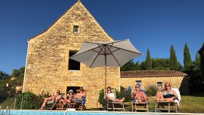 Edificio de piedra con zona de piscina, incluyendo sillones de descanso y una sombrilla.