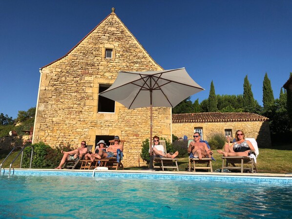 A stone building with a pool area, including lounge chairs and an umbrella.