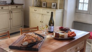 Una mesa de madera con tabla de cortar, botella de vino, copas y un plato de comida.