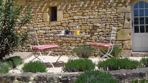 Un edificio de piedra con tejado de baldosas, una ventana pequeña y una puerta. Hay una mesa con sillas y una botella de jugo.