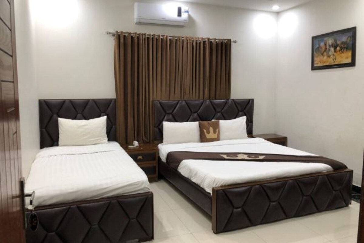 A hotel room with two beds, a nightstand, a curtain, and a painting on the wall.