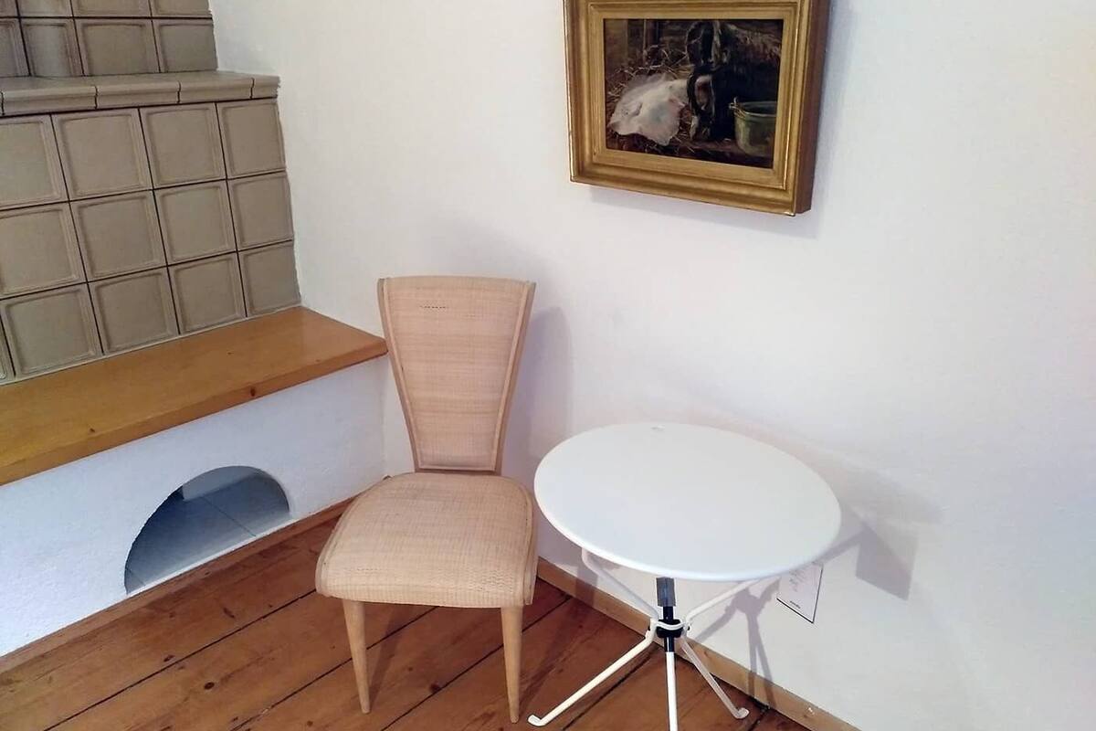 A corner room with a wooden bench, a white chair, and a small white table.