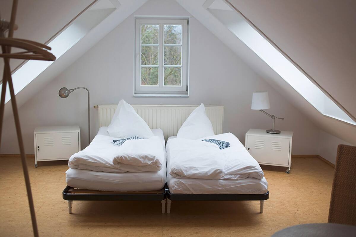 A twin bed with white bedding in a room with sloped ceilings and a skylight.
