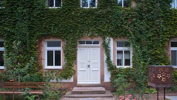 A building with a white door, a bench, and a garden with pink flowers. - Die Burg Schöna - In a national park (Reinhardtsdorf-Schoena)
