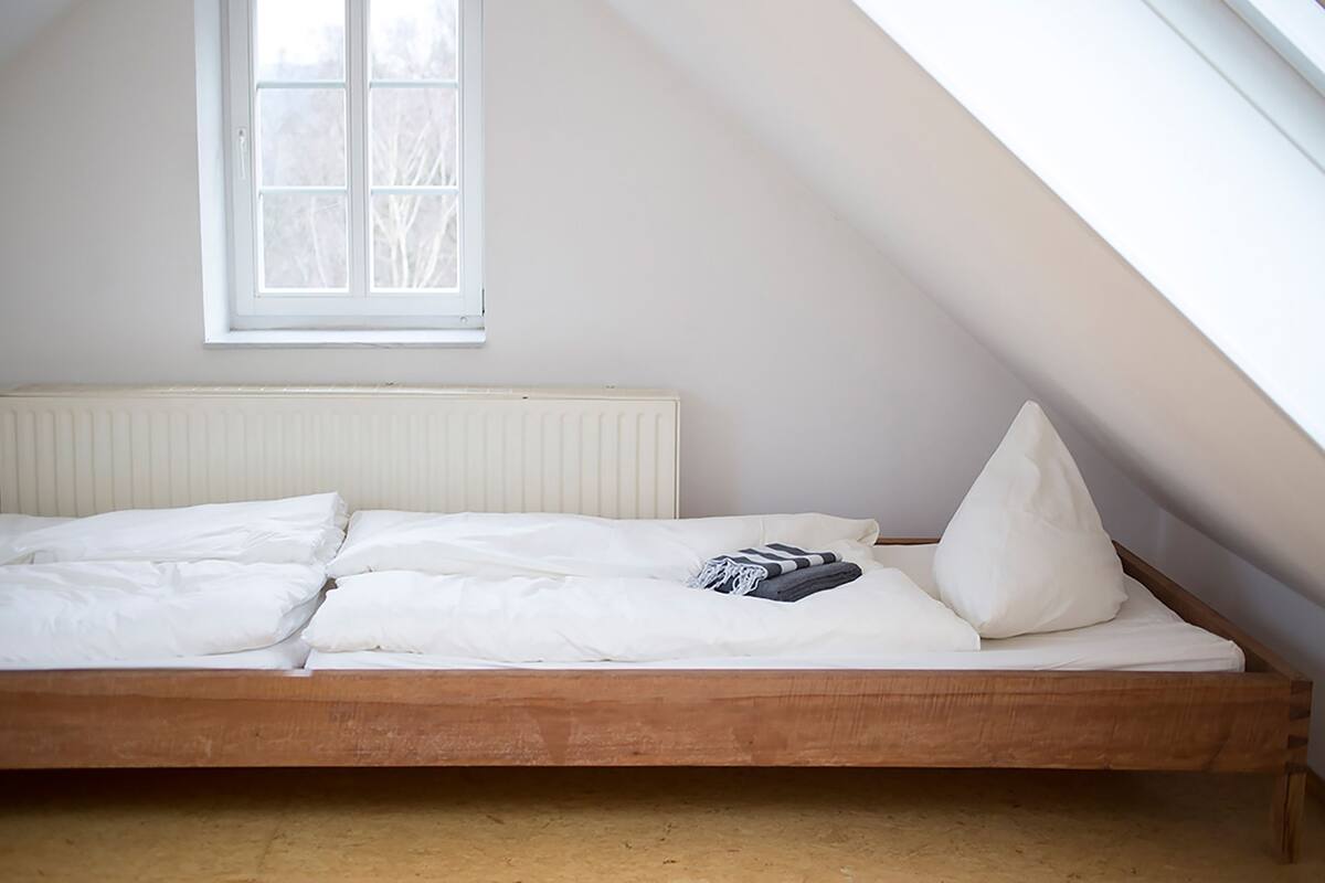 A single bed in a room with a sloped ceiling, a window, and a radiator.