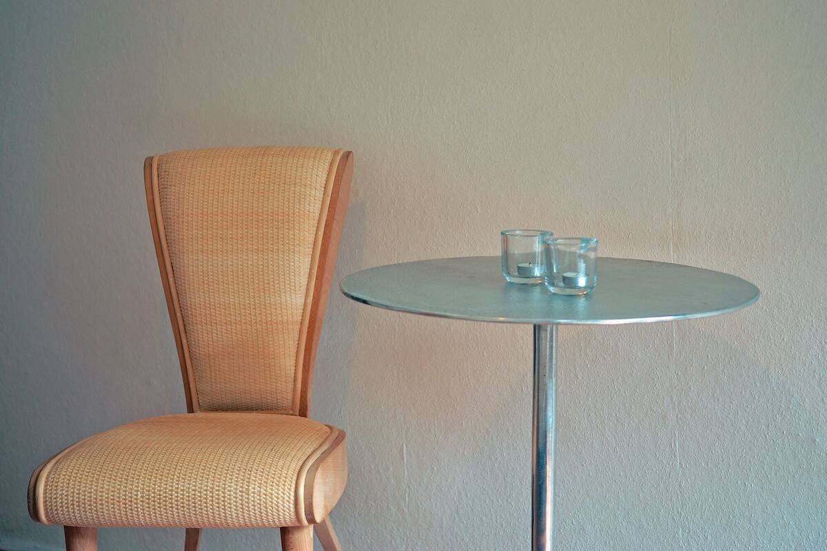 A wicker chair and a round table with two glasses on it.