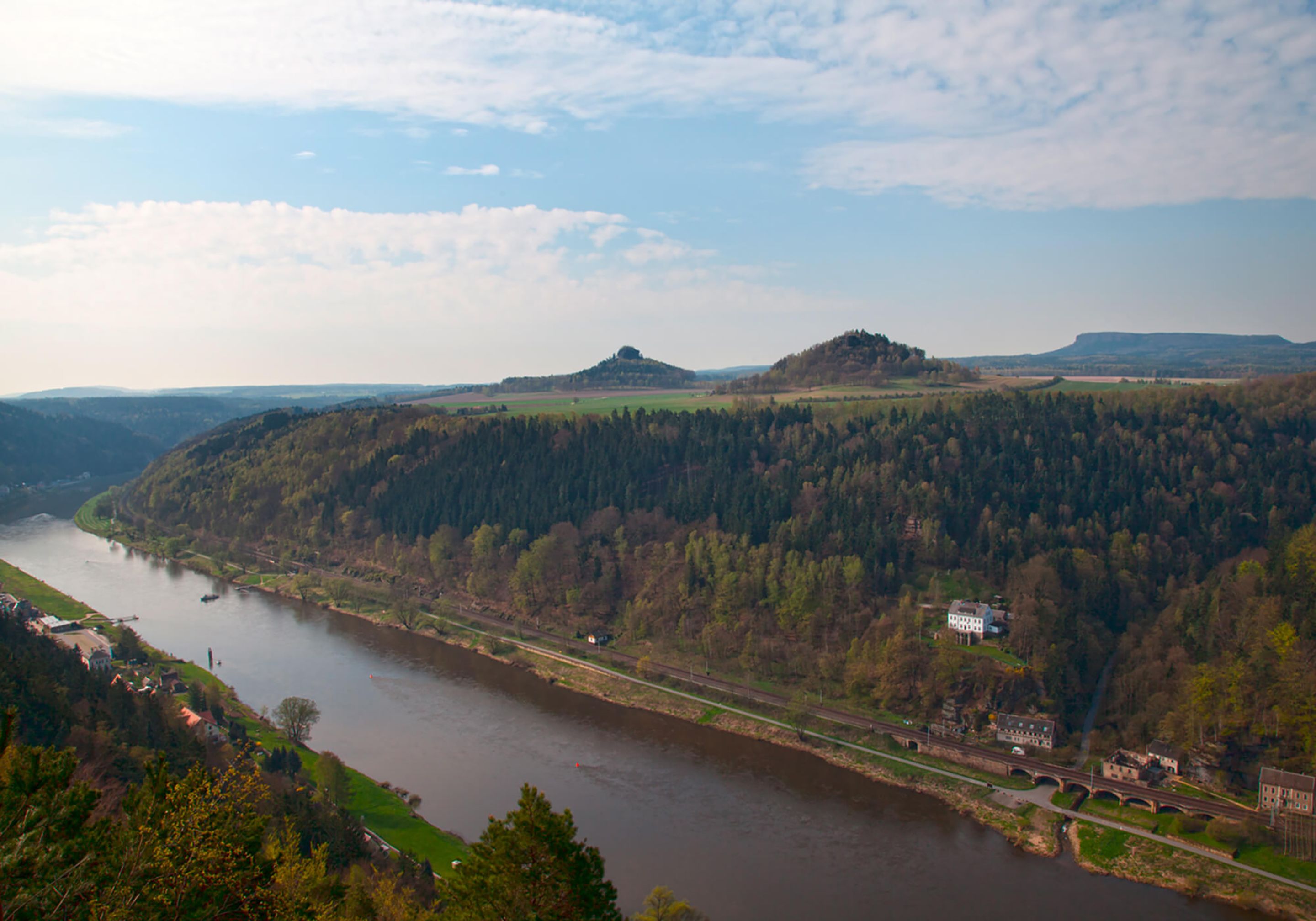 A river flowing through a valley with hills and a bridge.
