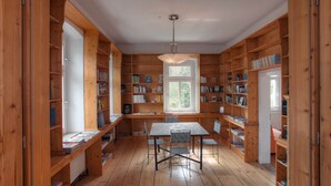 A spacious library with wooden bookshelves, a central table with chairs, and a large window providing natural light. - Die Burg Schöna - In a national park (Reinhardtsdorf-Schoena)
