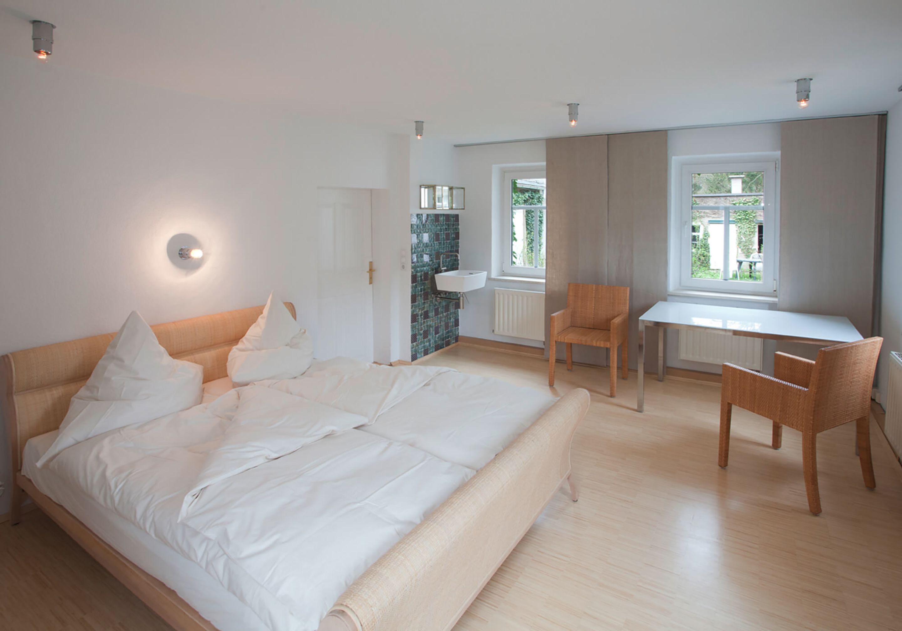 Un dormitorio con una cama grande, un escritorio y una silla. Una ventana proporciona luz natural.