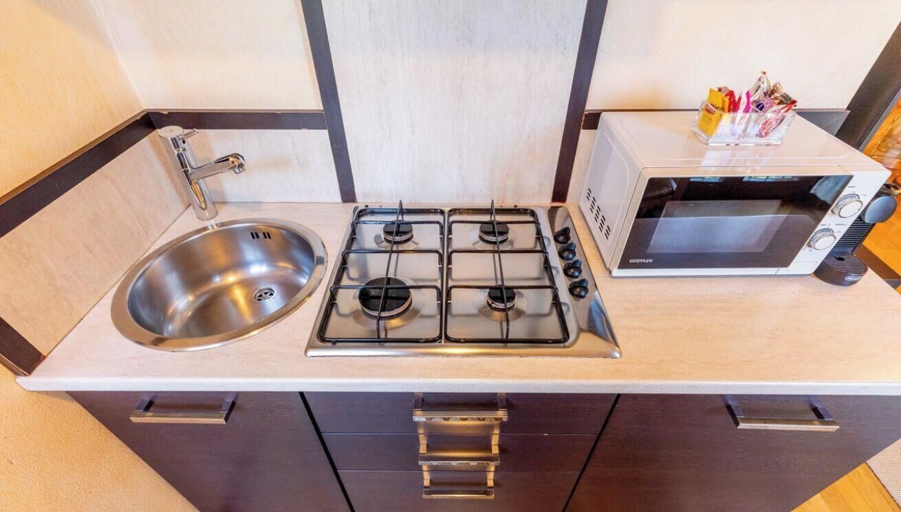 A compact kitchenette with a stainless steel sink, a gas stove with four burners, and a built-in microwave.