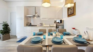 Une cuisine moderne avec des meubles blancs, une table à manger dressée avec de l’assiette bleue et un luminaire suspendu.