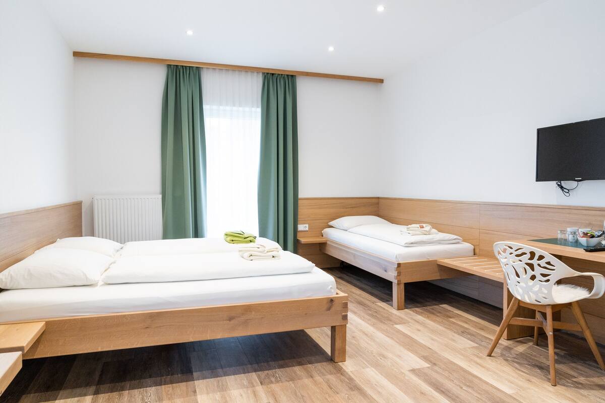 A modern hotel room with two beds, a desk, a chair, and a TV mounted on the wall.