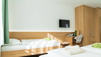 A hotel room with two beds, a TV mounted on the wall, wooden cabinets, and a desk with a chair.