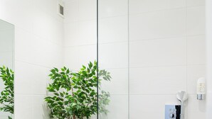 Un baño moderno con cabina de ducha de vidrio, una planta en maceta y un revestimiento de baldosas blancas.