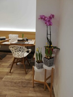 A modern interior with a wooden dining table, a white chair with a unique cut-out design, and a wall-mounted plant stand holding three potted plants. - Flöckner B & B (Salzburg)