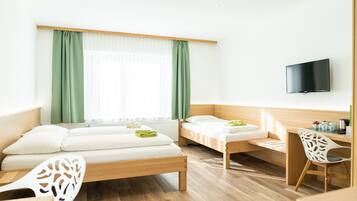 Une chambre d’hôtel moderne avec deux lits simples, un bureau en bois, une chaise, un téléviseur à écran plat et une grande fenêtre avec des rideaux verts.