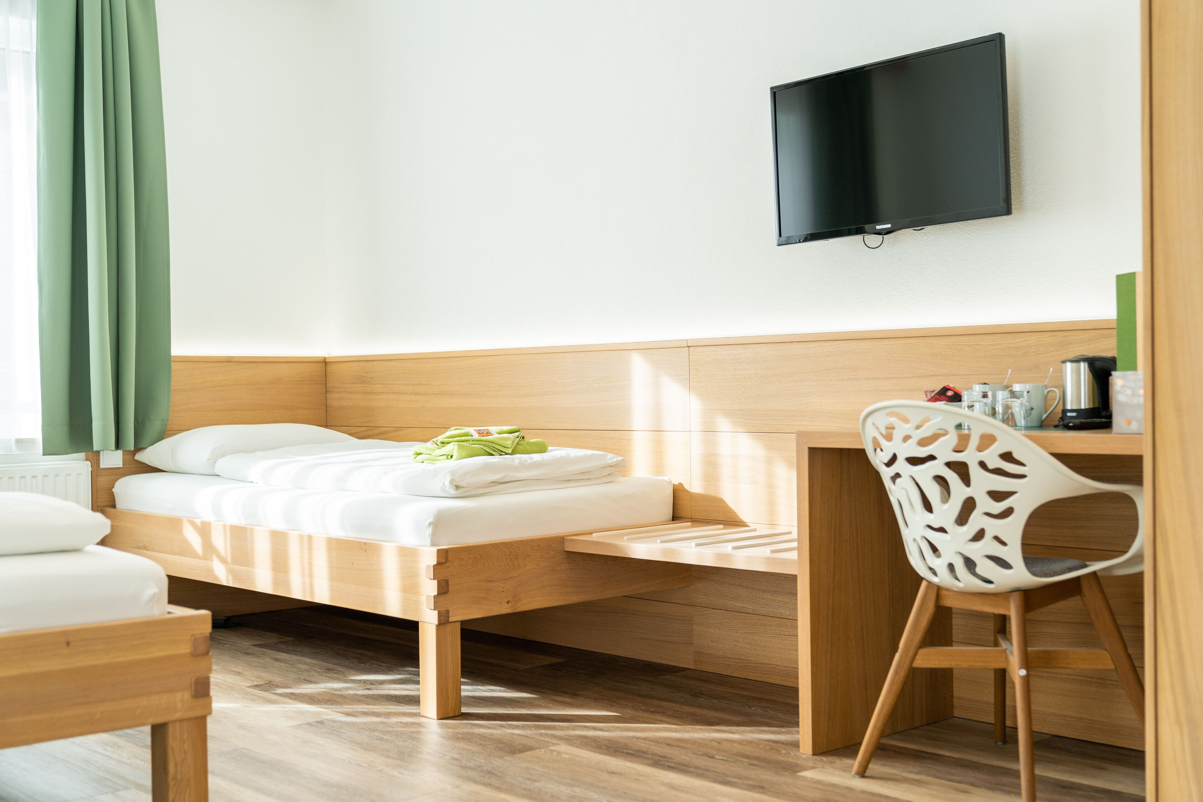 Una cama individual con cabecera de madera, una mesita de noche, una silla y un televisor de pantalla plana montado en la pared.