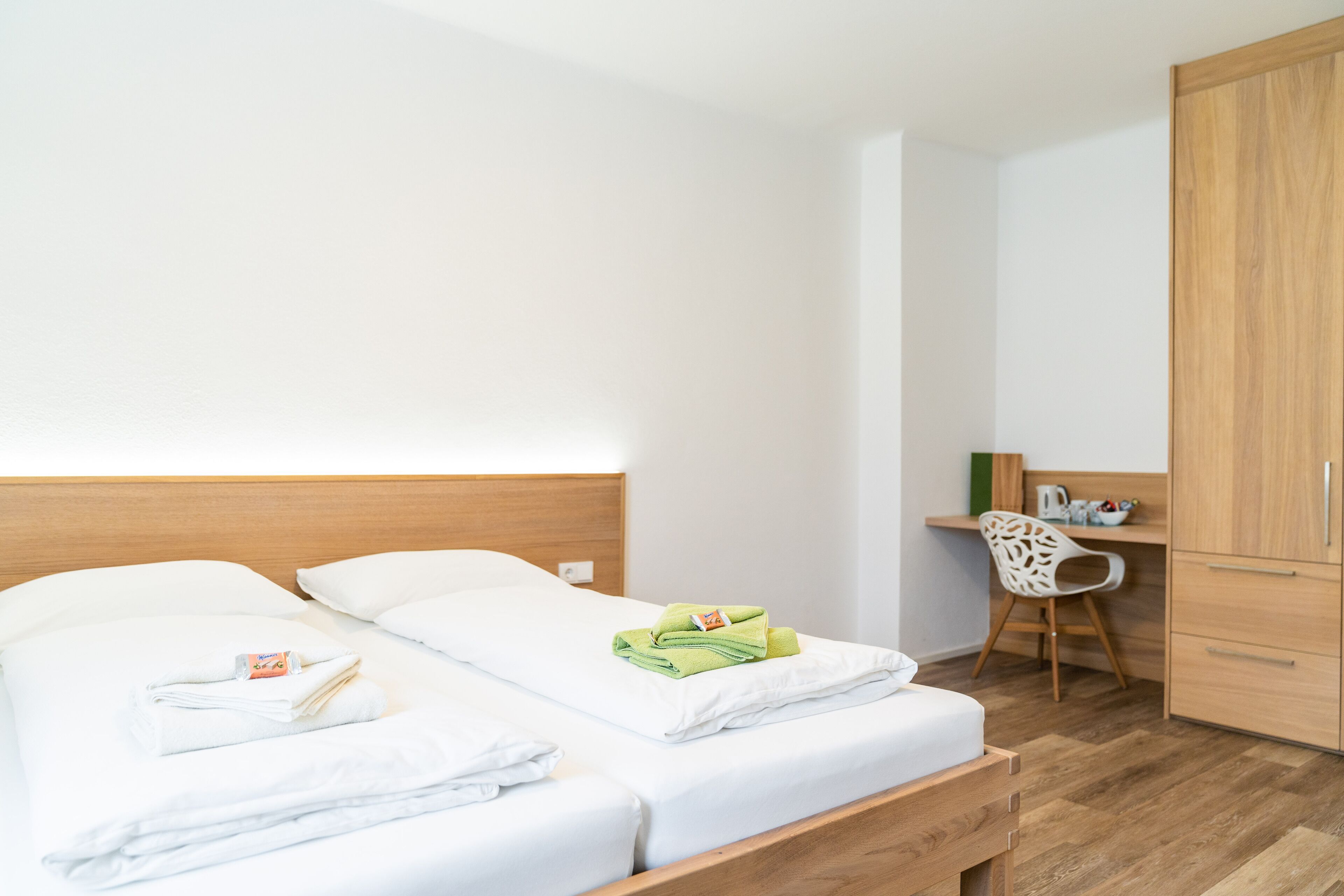 A hotel room with a wooden bed, white linens, a desk with a chair, and a wardrobe.