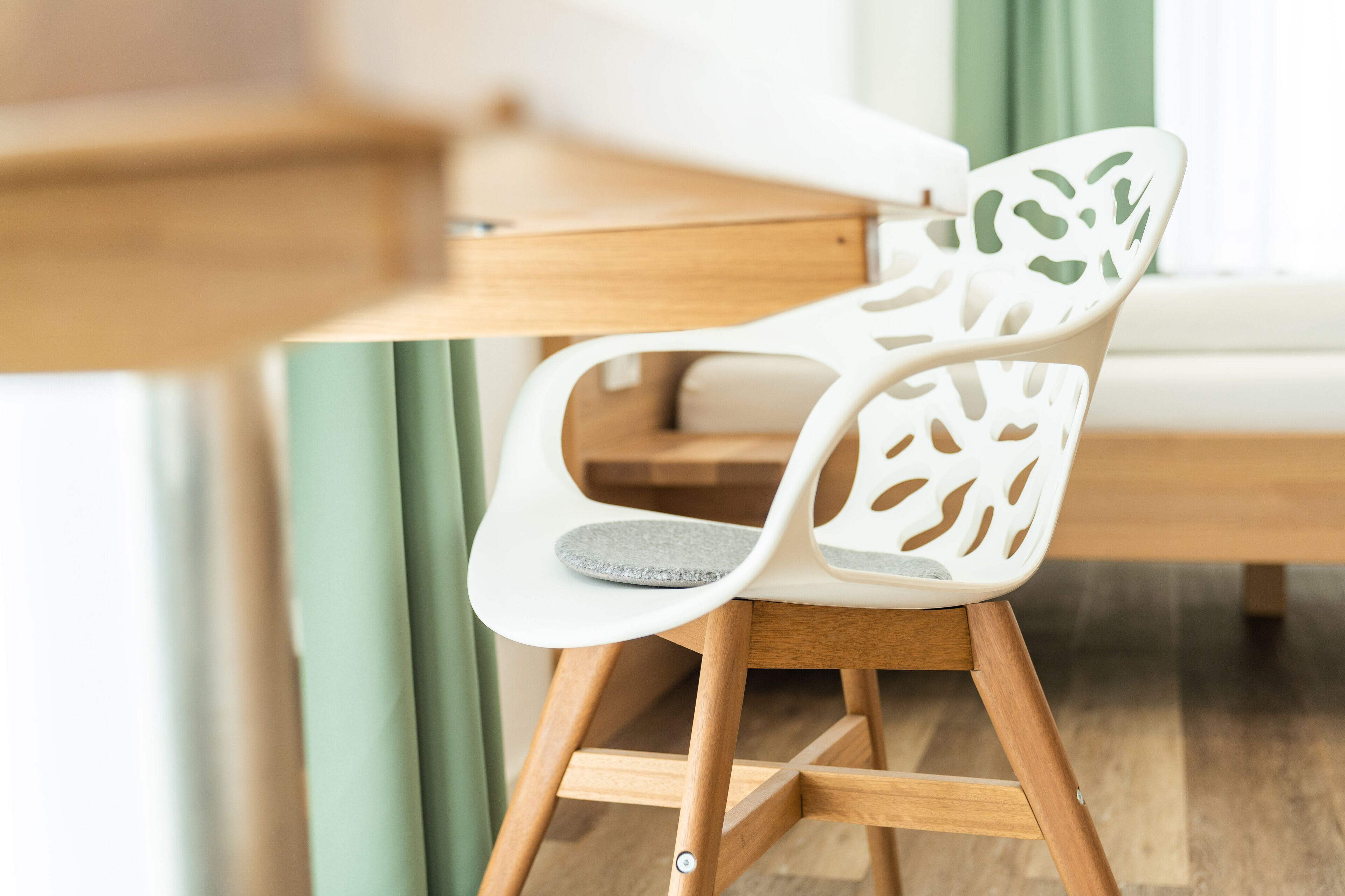 Une chaise blanche ornée d’un motif de feuilles sur le dossier, avec un coussin gris et des pieds en bois.