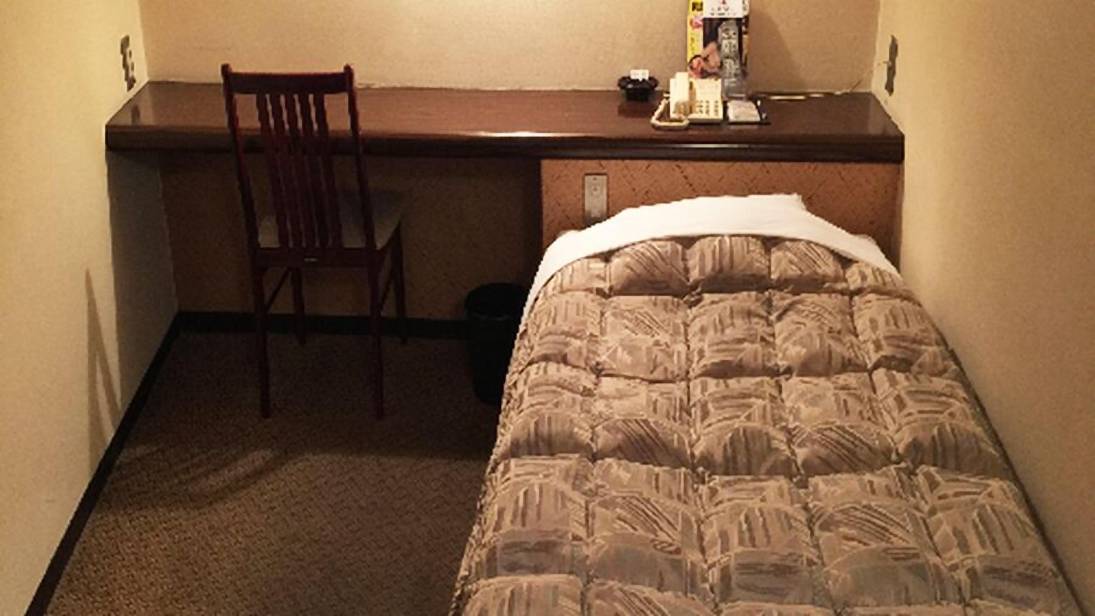 A small hotel room with a bed, a desk, and a chair.