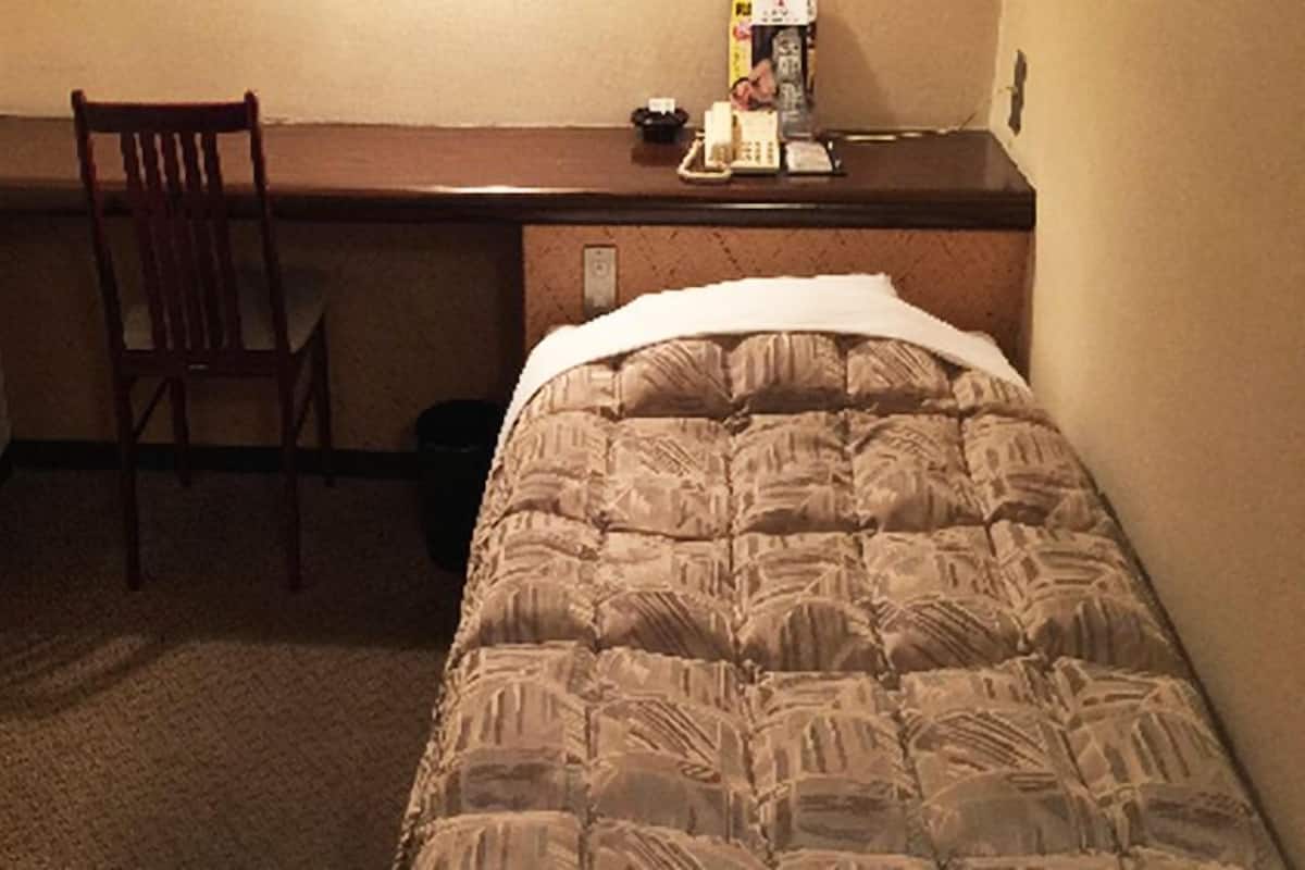 A small hotel room with a bed, a desk, and a chair.