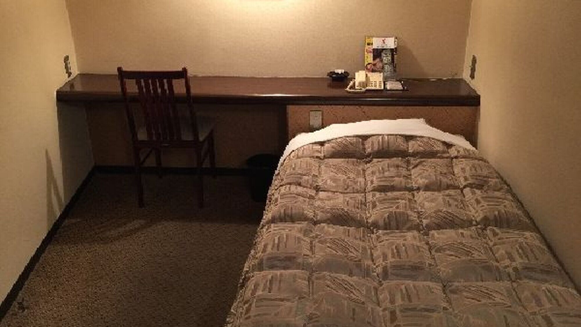 A small hotel room with a single bed, a desk, and a chair.
