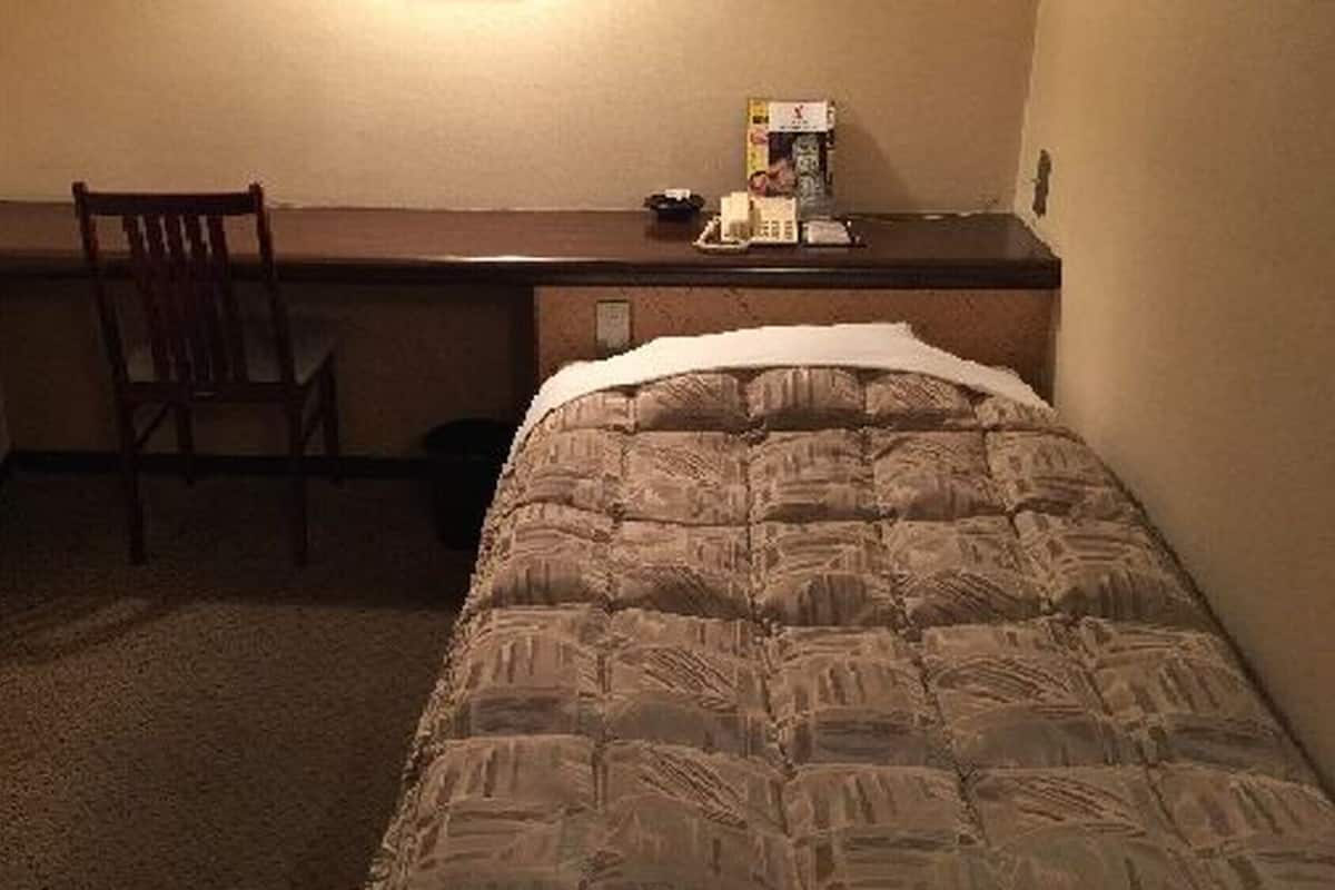 A small hotel room with a single bed, a desk, and a chair.