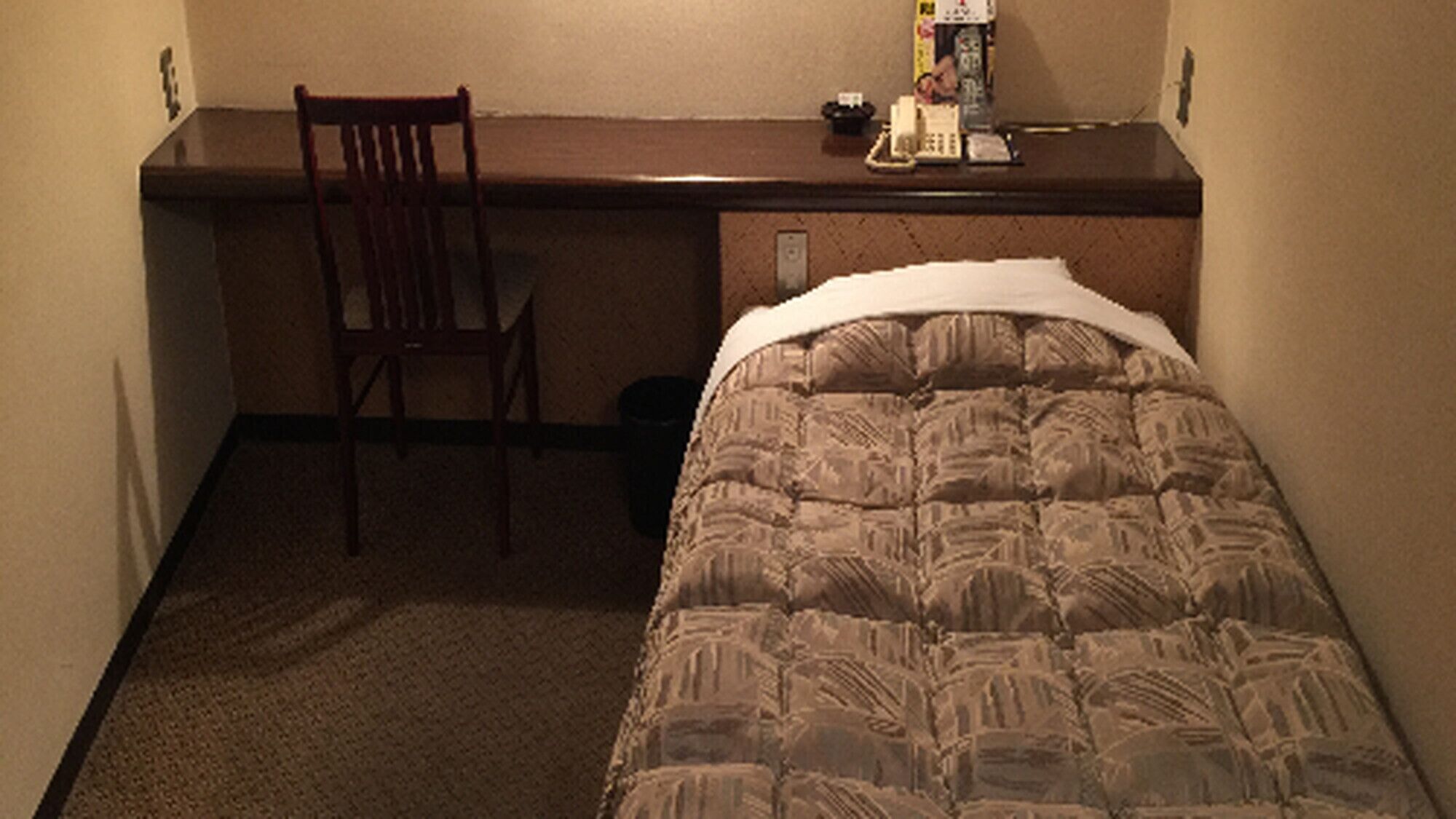 A hotel room with a bed, a chair, a desk, and a small table with items on it.