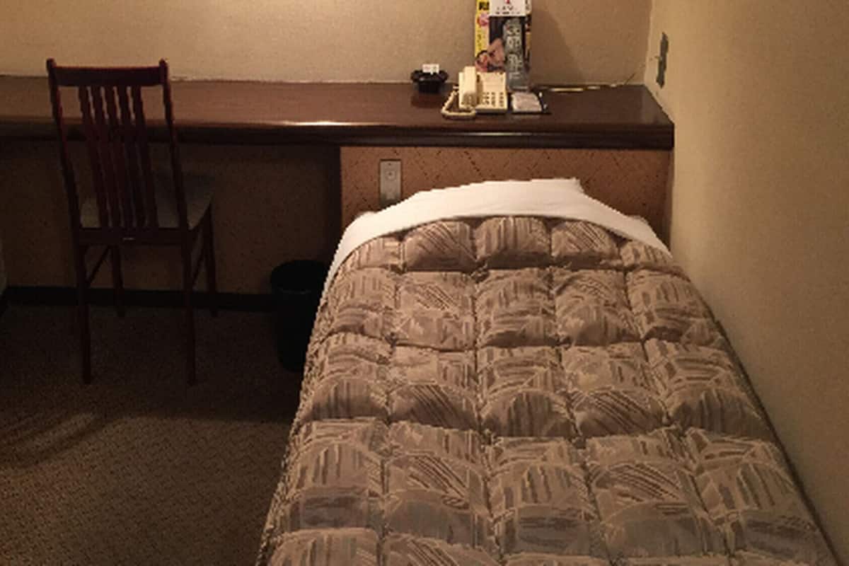 A hotel room with a bed, a chair, a desk, and a small table with items on it.