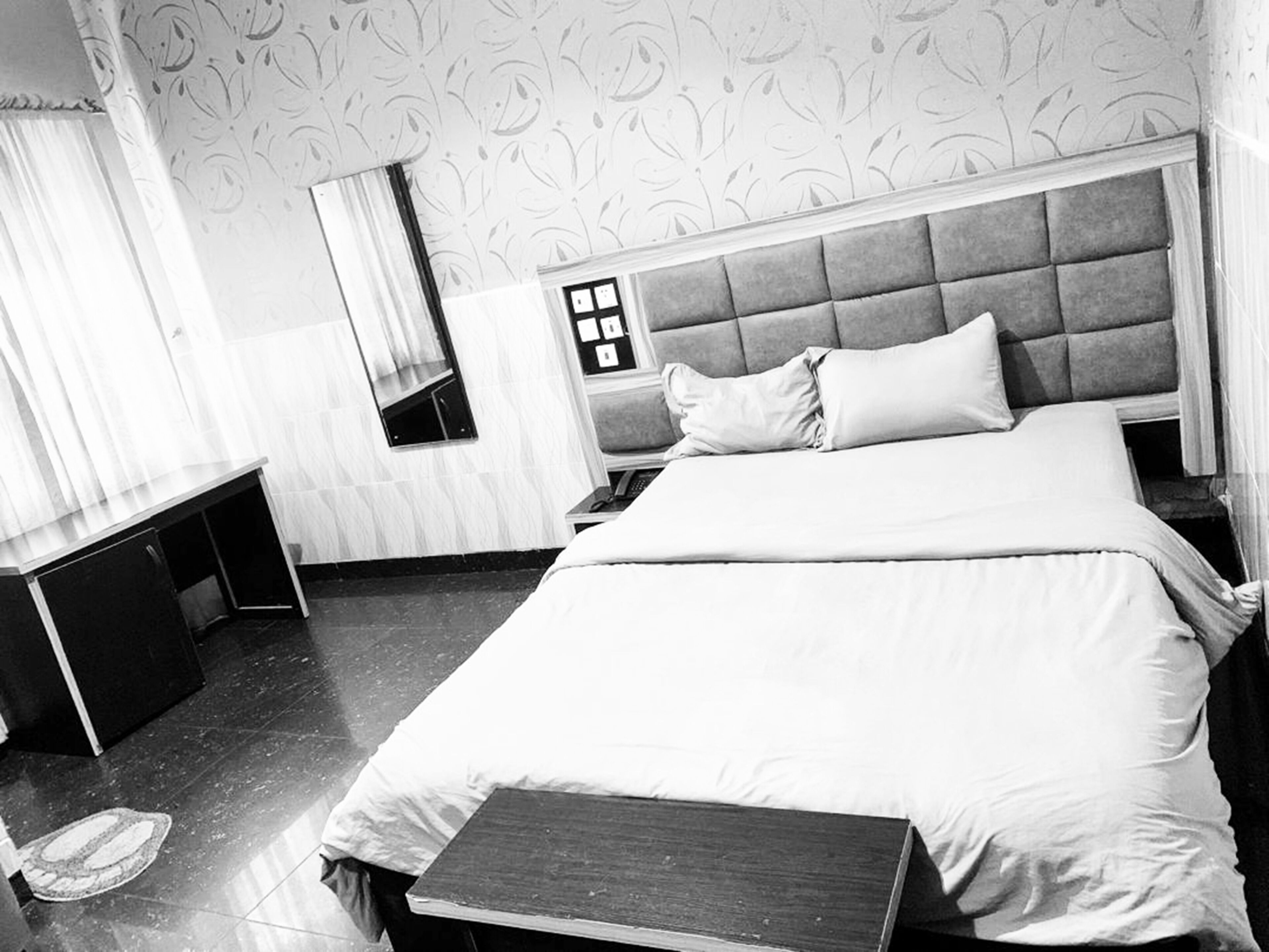 Habitación de hotel con una cama grande, una mesita de noche, un espejo y una ventana con cortinas.